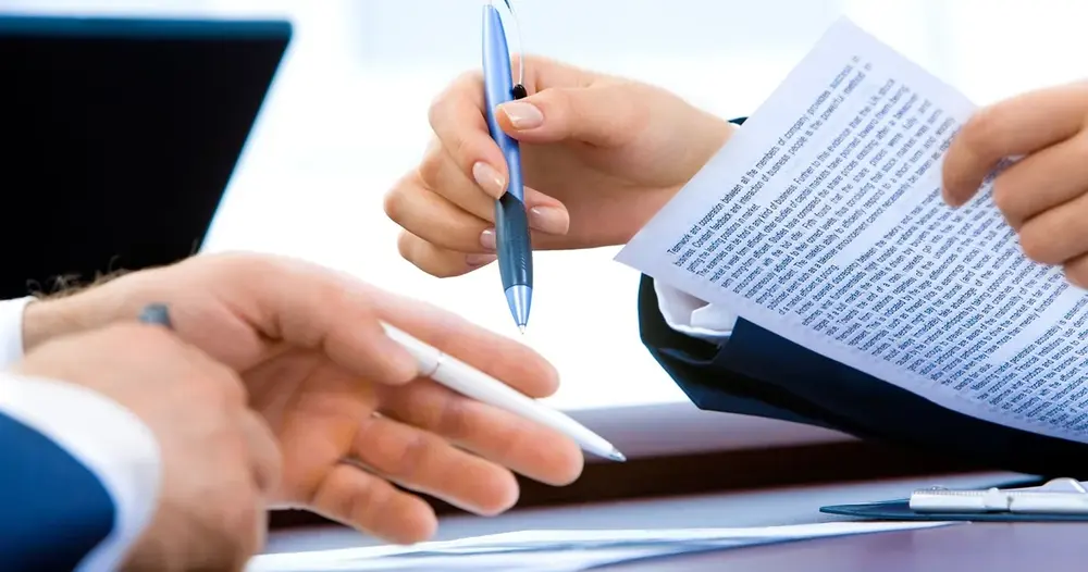 Mãos assinando um documento com caneta sobre a mesa de trabalho